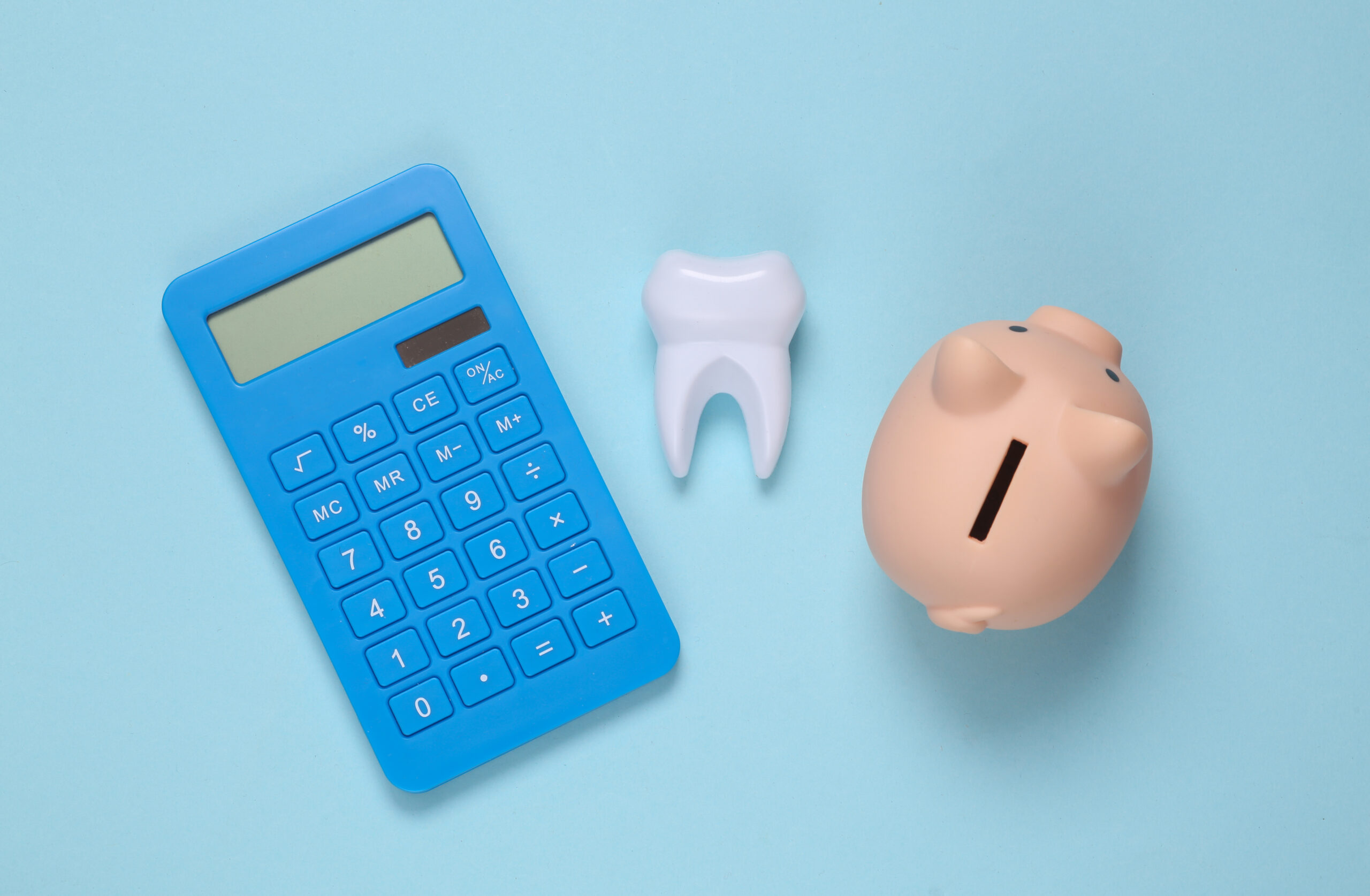 Dental treatment costs. Piggy bank, calculator and tooth on blue background. Top view